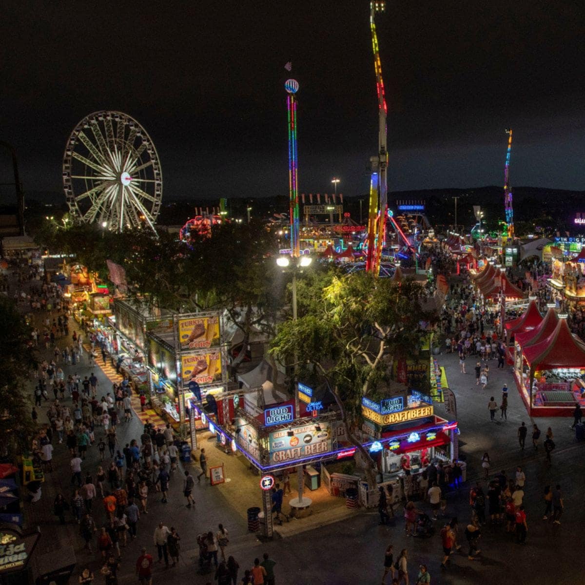 A county fair midway after dark, its Ferris wheel and rides lit above the crowds