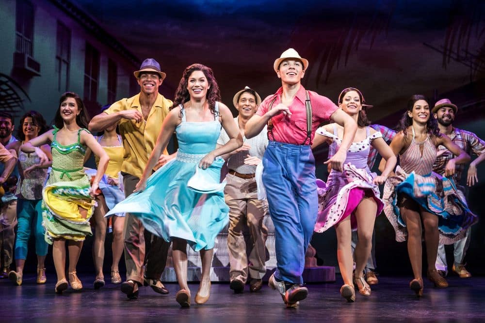 Dancers in bright summer costumes mid-number across a theatre stage